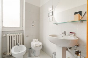 Un bany modern amb bidet, vàter, rentapel obert i prestatge de vidre.