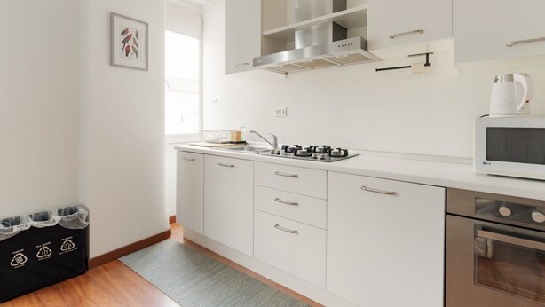 Een moderne keuken met witte kasten, roestvrijstalen apparatuur en een raam dat voor natuurlijk licht zorgt.