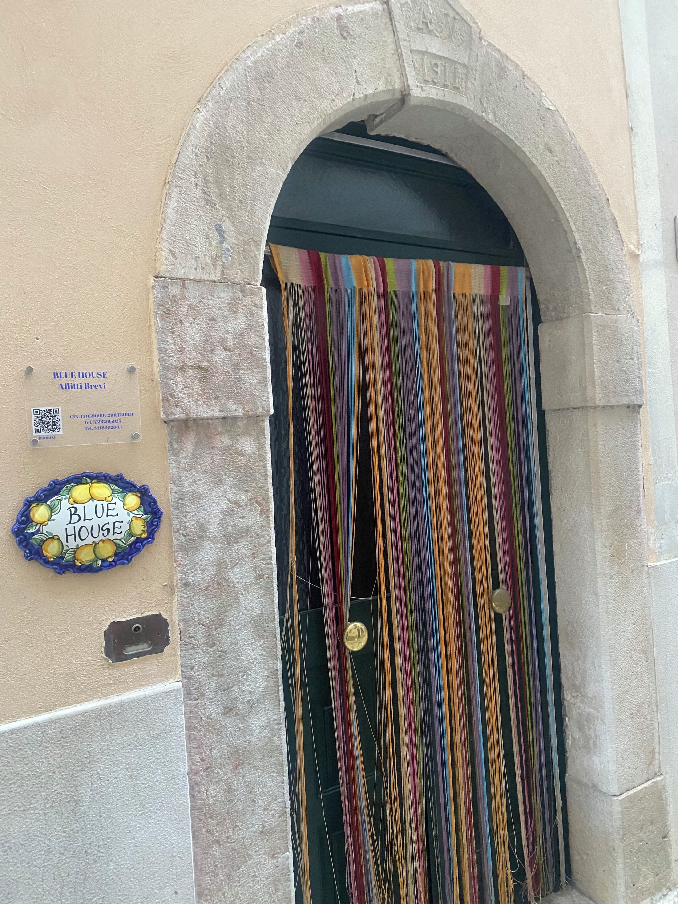 Una entrada de edificio con un arco de piedra, una cortina a rayas de colores y un letrero azul en la pared.