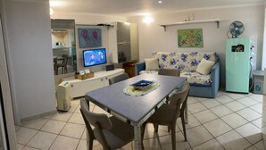 A living room with a dining table, chairs, a sofa, a television, and a refrigerator. - Blue House: A beautiful and charming little house in the neighborhoods along Via dell'Indipendenza (Gaeta)