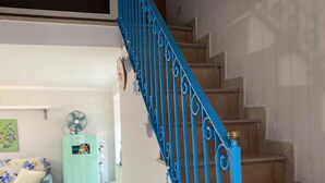 Una escalera con barandas azules que conduce a un piso superior, un refrigerador azul claro, una mesa de comedor con sillas y un reloj en la pared.