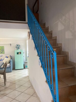A staircase with blue railings leading to an upper floor, a light blue refrigerator, a dining table with chairs, and a clock on the wall. - Blue House: A beautiful and charming little house in the neighborhoods along Via dell'Indipendenza (Gaeta)