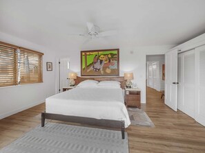 A bedroom with a bed, two bedside tables with lamps, a ceiling fan, a painting on the wall, and a door leading to another room. - Partial Ocean View Suite w/Full Kitchen, W/D, WiFi, Lanai, TV Kanaloa 3401 (KAILUA-KONA)