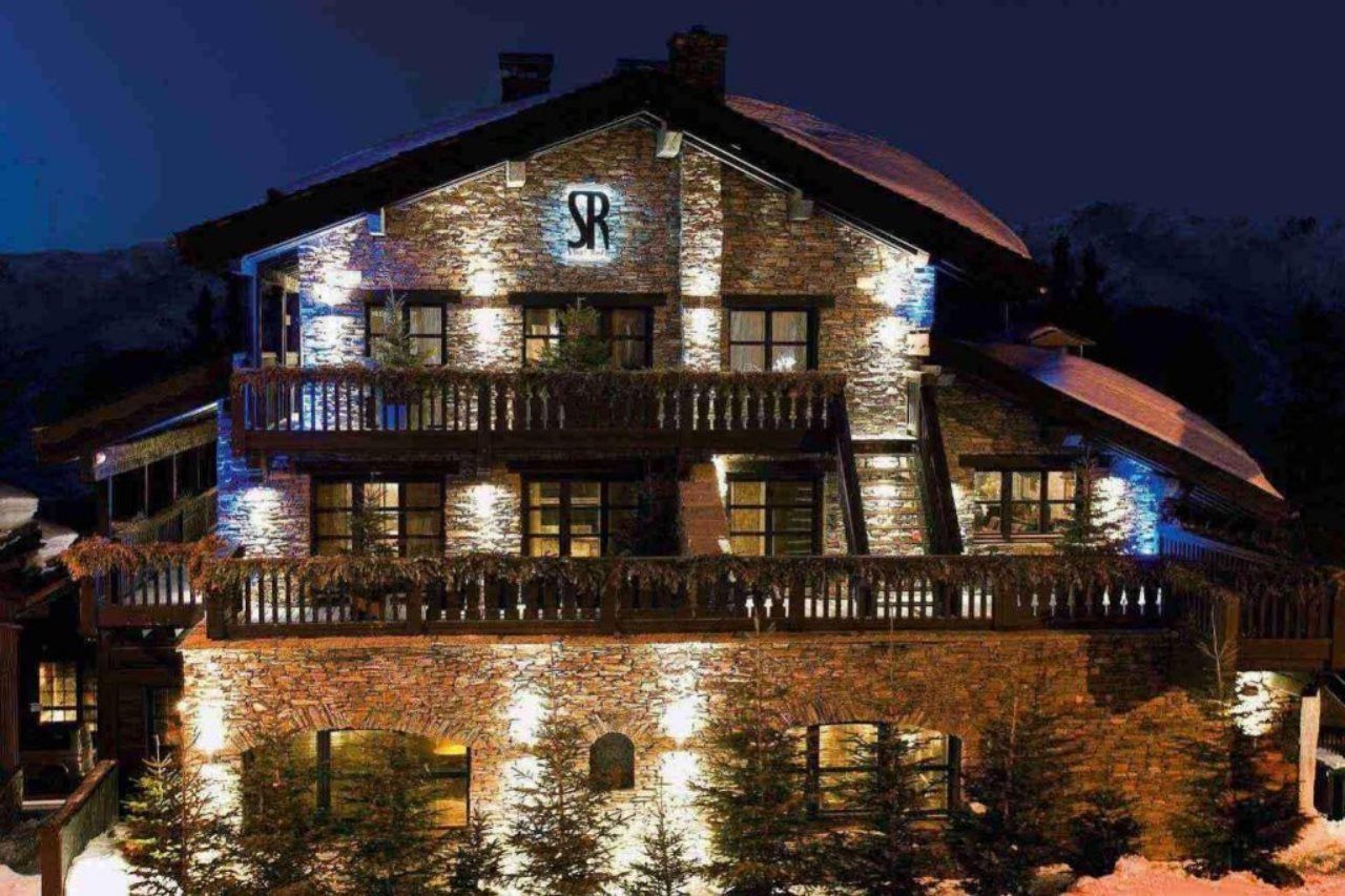 A multi-story stone building with a prominent 'SR' logo, balconies, and a reflective water feature in front.
