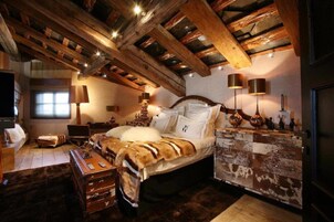 A rustic bedroom with exposed wooden beams, a bed with white linens, a wooden dresser, and a television.