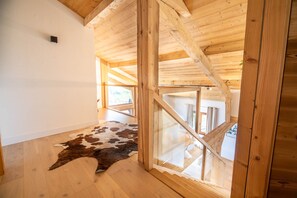 A room with wooden beams, a cowhide rug, and a glass door leading to another space. - The Black Stag: Finnish sauna, mountain view, sleeps 8 (La Bresse)
