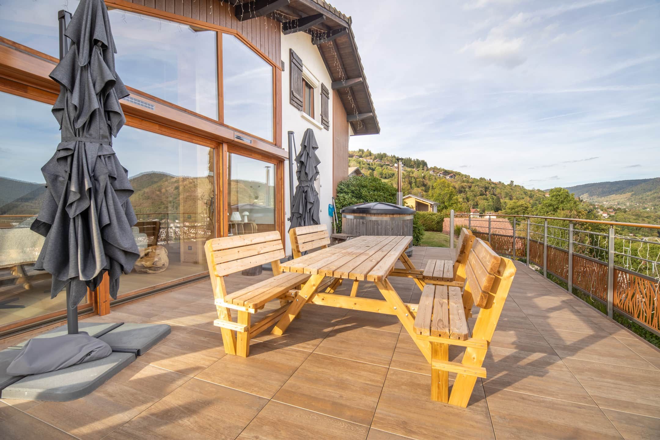 Een houten terras met een picknicktafel en stoelen, een jacuzzi en uitzicht op een heuvel.