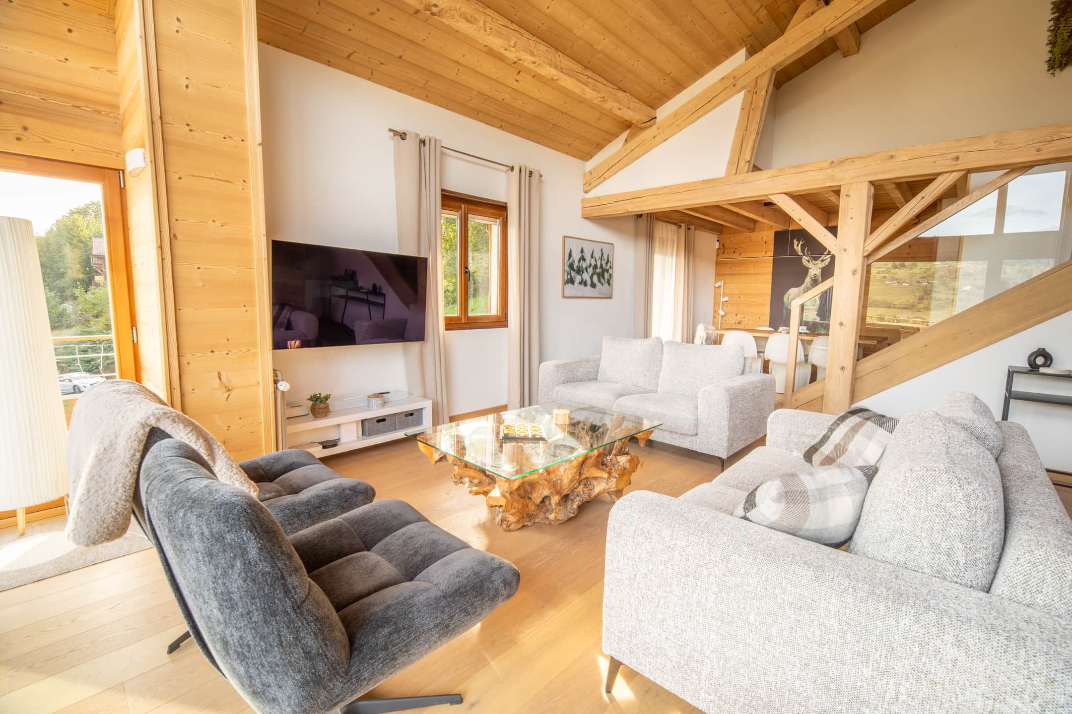 Ein geräumiges Wohnzimmer mit hoher Decke, Holzbalken, einem großen Flachbildfernseher und einer gemütlichen Sitzecke mit einem außergewöhnlichen Couchtisch.