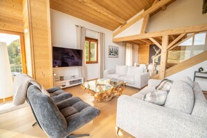 A spacious living room with a high ceiling, wooden beams, a large flat-screen TV, and a cozy seating area with a unique coffee table. - The Black Stag: Finnish sauna, mountain view, sleeps 8 (La Bresse)