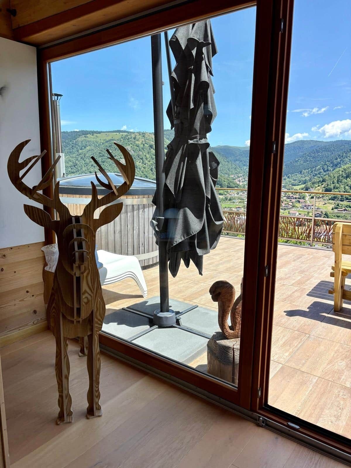 Ein Zimmer mit einem großen Fenster, einer Holz-Hirschskulptur und Blick auf eine gebirgige Landschaft.