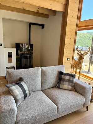 Ein gemütliches Wohnzimmer mit einem grauen Sofa, zwei karierten Kissen, einem Kamin und einer Hirschskulptur.