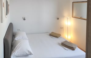 Ein Hotelzimmer mit einem Einzelbett, zwei Kissen, einer Nachttischlampe und einem Spiegel an der Wand.