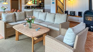 Ein gemütliches Wohnzimmer mit einer Couch, einem Couchtisch, Korbstühlen, einem Kamin und einer Küche im Hintergrund.