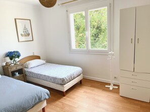 Ein Schlafzimmer mit Bett, Nachttisch, Lampe und einem Fenster mit Blick auf Grünflächen.