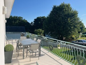 Ein Balkon mit Tisch, Stühlen, einem Grill und einem Geländer mit Bepflanzung.