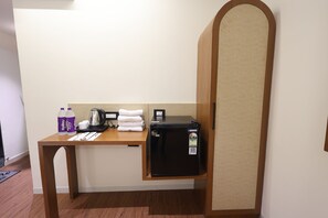 A hotel room with a wooden desk, a black refrigerator, a kettle, a stack of white towels, and two bottles of Bailey's Pure Pura water. - Hotel Heaven Green (Rajkot)