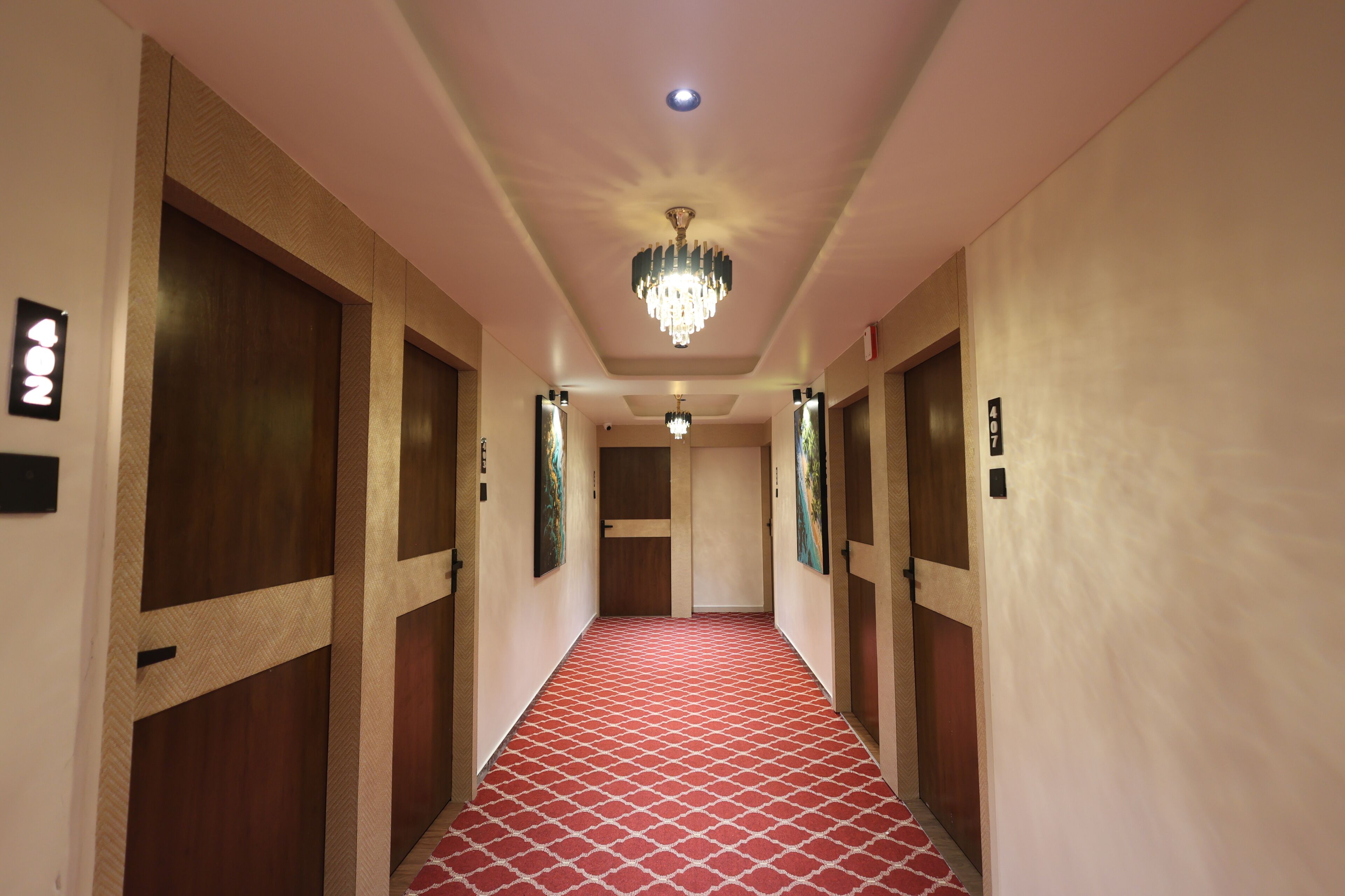 Un couloir d’hôtel avec un tapis rouge à motifs, des portes en bois et un lustre.