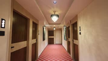 Un couloir d’hôtel avec un tapis rouge à motifs, des portes en bois et un lustre.
