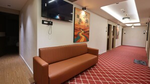 Eine Hotelhalle mit einer Couch, einem Flachbildfernseher, einem Palmen-Gemälde und einem roten Teppich mit Muster.