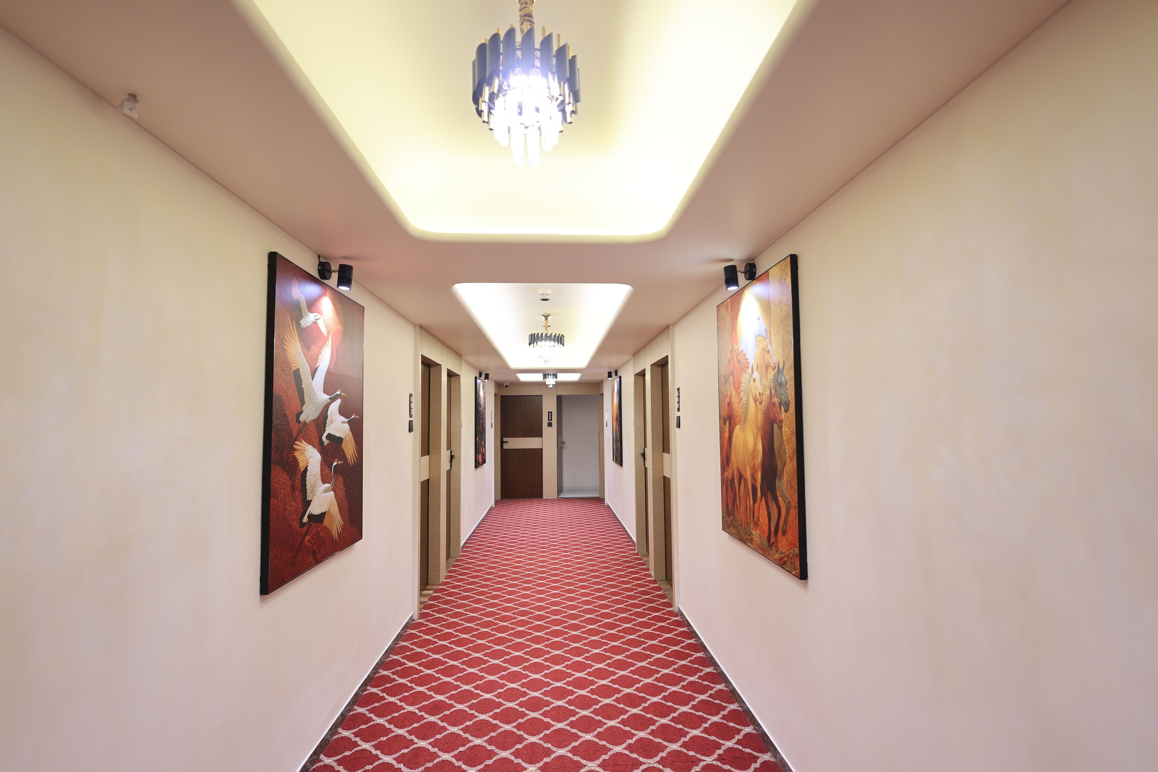 A hotel hallway with a red patterned carpet, a chandelier, and artwork on the walls.