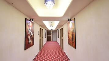 A hotel hallway with a red patterned carpet, a chandelier, and artwork on the walls.