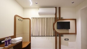 Ein Hotelzimmer mit einer hölzernen Bank, einem an der Wand befestigten Fernseher, einer Klimaanlage und einem mit Vorhängen versehenen Fenster.