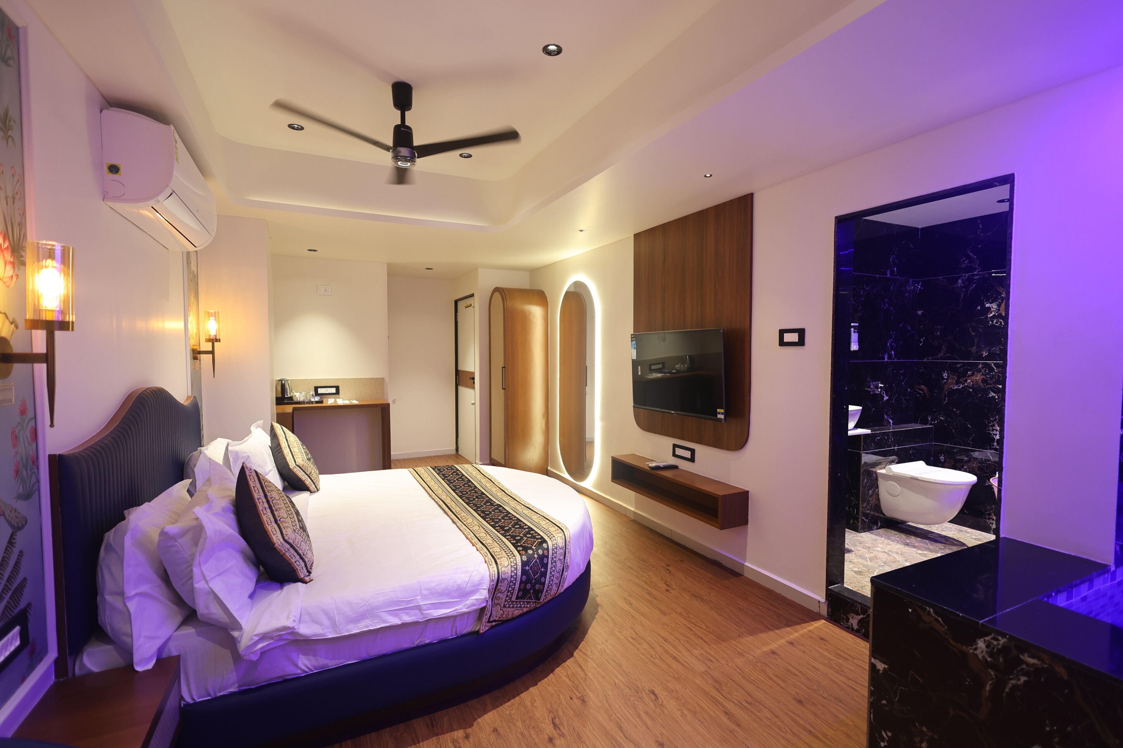 Un dormitorio moderno con una cama curvada, ventilador de techo, televisor y baño con encimera de mármol.
