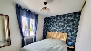 Quarto com cama, cabeceira, mesa de cabeceira, luminária, janela com cortinas e parede com padrão geométrico.
