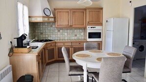 Cozinha compacta com armários de madeira, fogão branco e uma mesa de jantar com cadeiras.