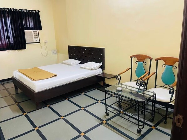 Una habitación con cama, una mesita con sillas, una ventana con cortinas y un equipo de aire acondicionado.