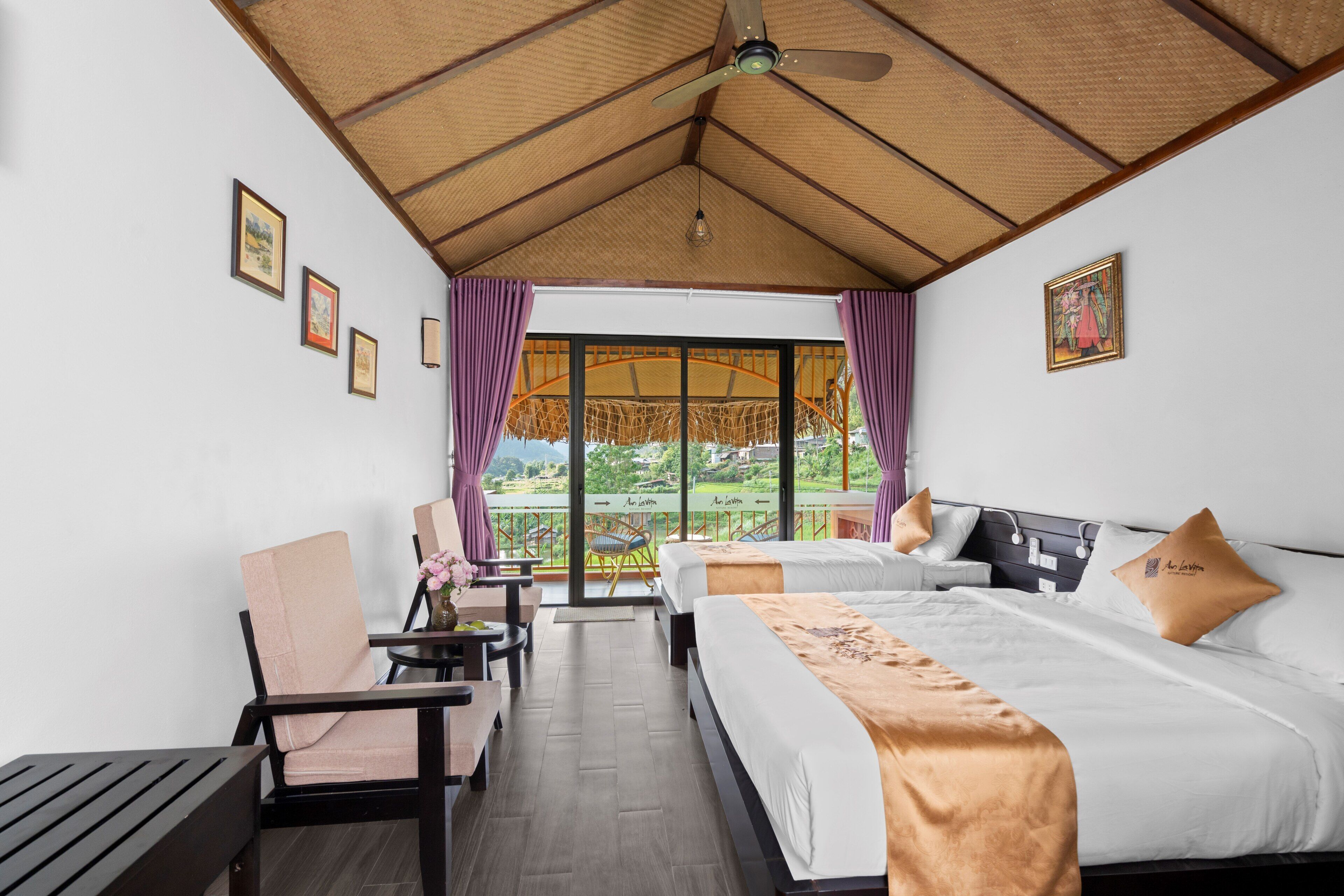 A hotel room with a bed, a chair, a table, and a view of a garden through a large window.