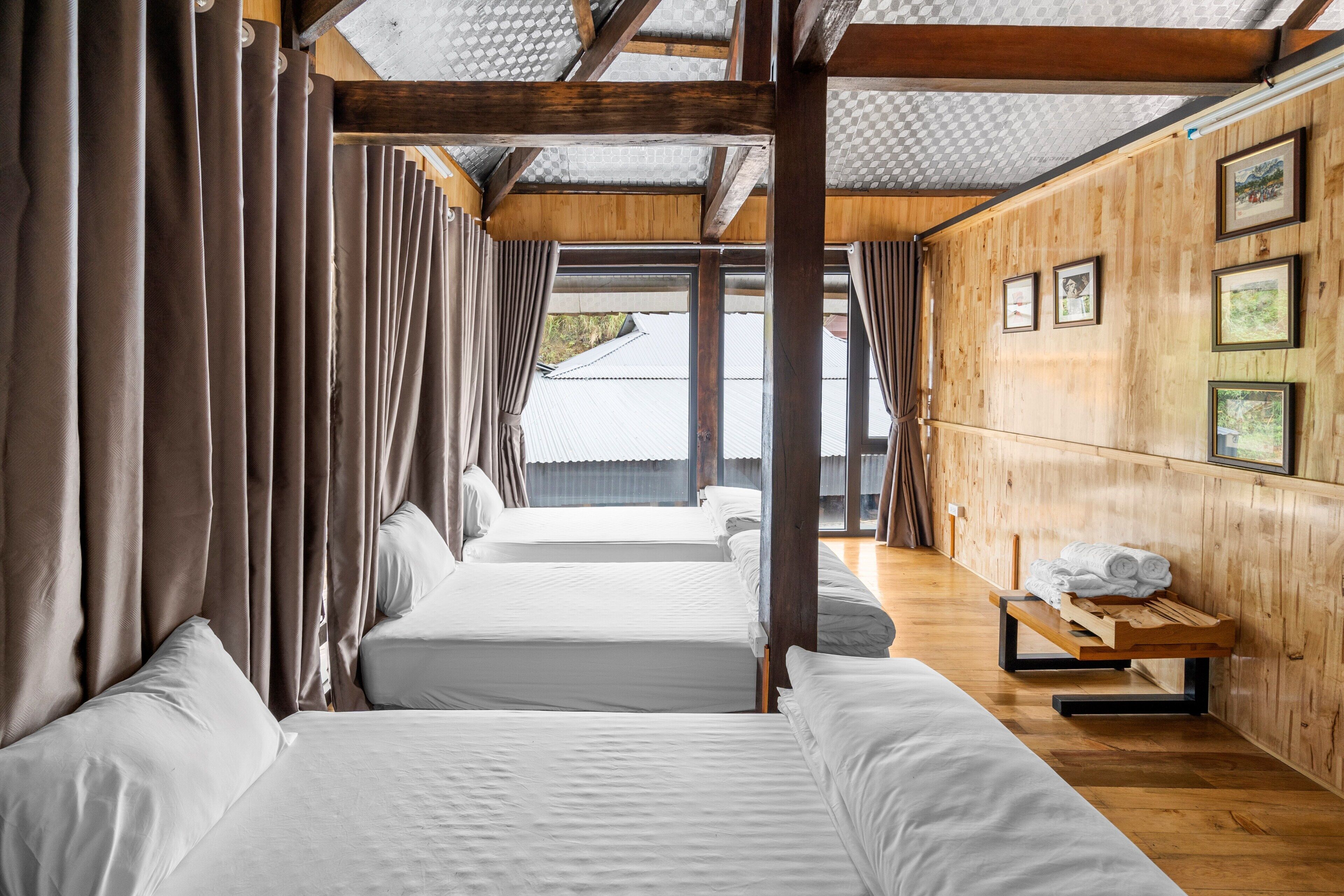 Habitación con tres camas, paredes de madera y un banco con toallas.