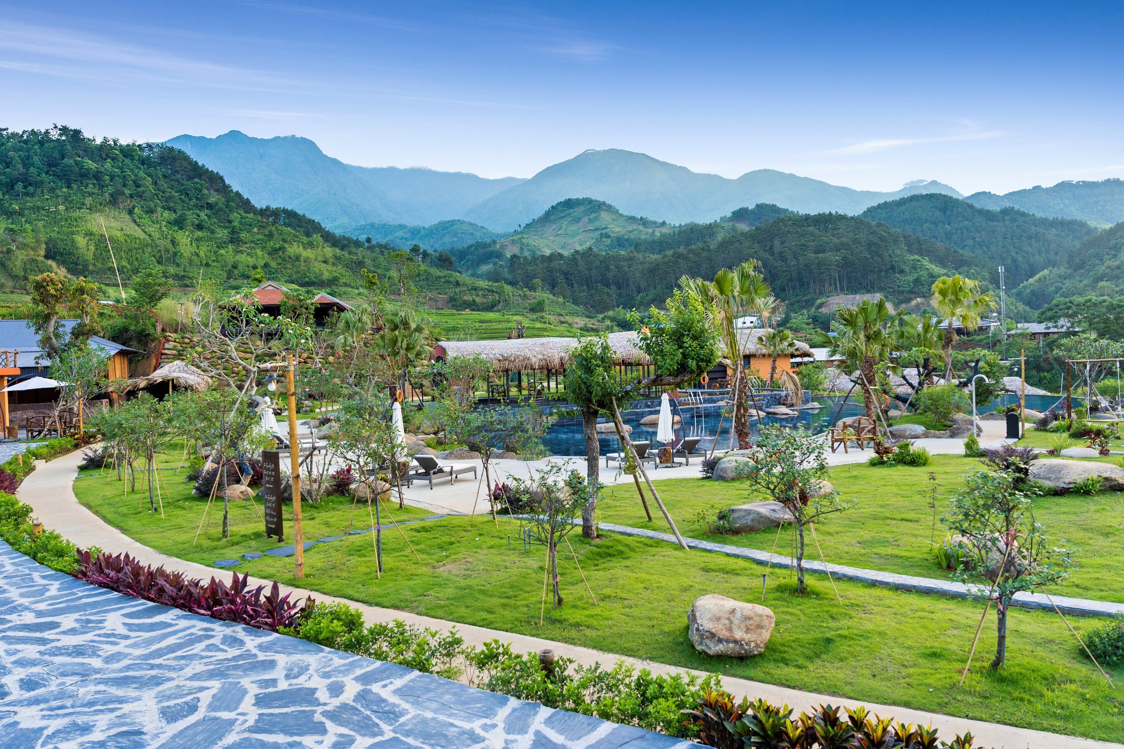 Un resort con piscina, edificios de techo de paja y exuberante vegetación.