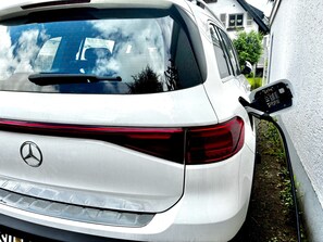 A white car parked with a charging station attached, a Mercedes-Benz logo, and a rear view of the vehicle. - Fiber-optic Internet, electric car charging station + garden + pool (Bad Honnef)
