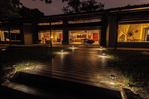 A modern house with a wooden deck, outdoor seating, and a well-lit interior.