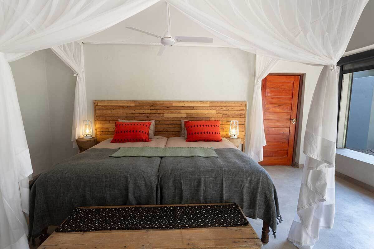 A bedroom with a canopy bed, a wooden headboard, bedside lamps, and a view of the outside.