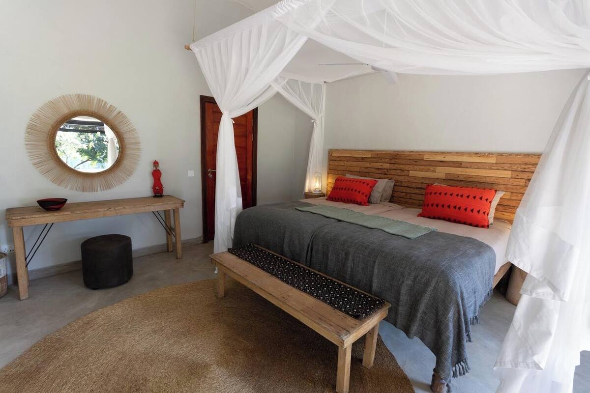 A bedroom with a canopy bed, a round mirror, a wooden bench, and a small table.
