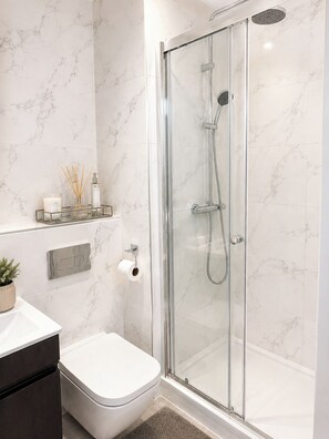 Ein modernes Badezimmer mit einer gläsernen Duschkabine, einer Toilette und einer Wand mit Marmorplatten.