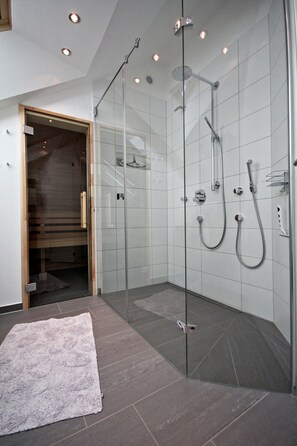 Eine moderne Dusche mit Glastüren, einem weißen Teppich und einer hölzernen Sitzbank.