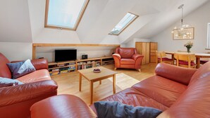 Amplio apartamento tipo loft con techos altos, tragaluces, una mesa de comedor de madera, sofás de cuero y un televisor.