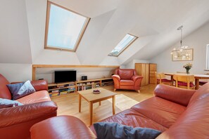 Ein geräumiges Lofty mit hohen Decken, Dachfenstern, einem Holzes Esstisch, Ledersofas und einem Fernseher.