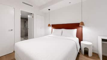A modern hotel room with a large bed, a bedside table, a nightstand, a shower area, and a wardrobe.