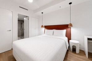 Una habitación de hotel moderna con una cama grande, una mesita de noche, una ducha y un armario.