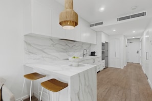 Uma cozinha moderna com bancadas de mármore, luminária pendente e banquetas de madeira.