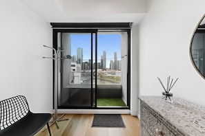 A modern room with a sliding glass door to a balcony, a black chair, a small table with a decorative item, and a patterned dresser. - Aerie Stays Wharf Collection (Docklands)