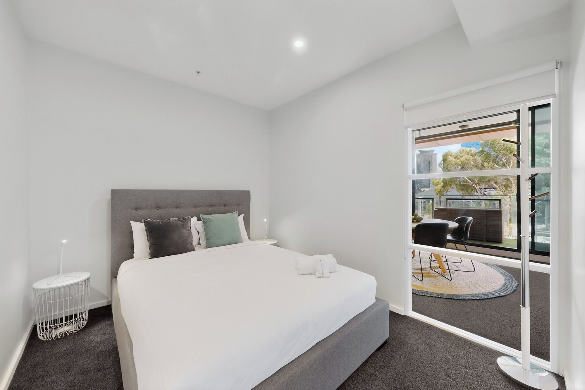 Une chambre d’hôtel moderne avec un grand lit, une tête de lit grise et une vue sur l’extérieur grâce à une porte-fenêtre coulissante.