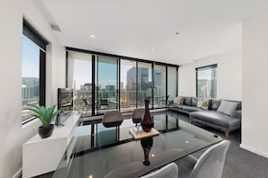 Uma sala de estar moderna com uma mesa de centro de vidro, um sofá e um espaço de jantar com tampo de vidro.
