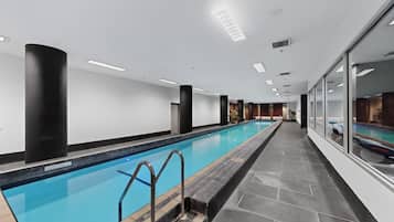 Uma piscina interior extensa, com chão em mosaico, colunas pretas e vista ampla da área da piscina.