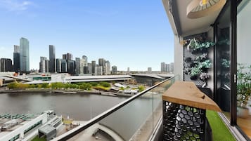 Uma varanda com vista para o horizonte da cidade, um rio e um edifício moderno com fachada de vidro.