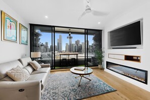 Una sala de estar moderna con sofá, mesa de centro, chimenea, televisor y vista a la ciudad a través de amplios ventanales.